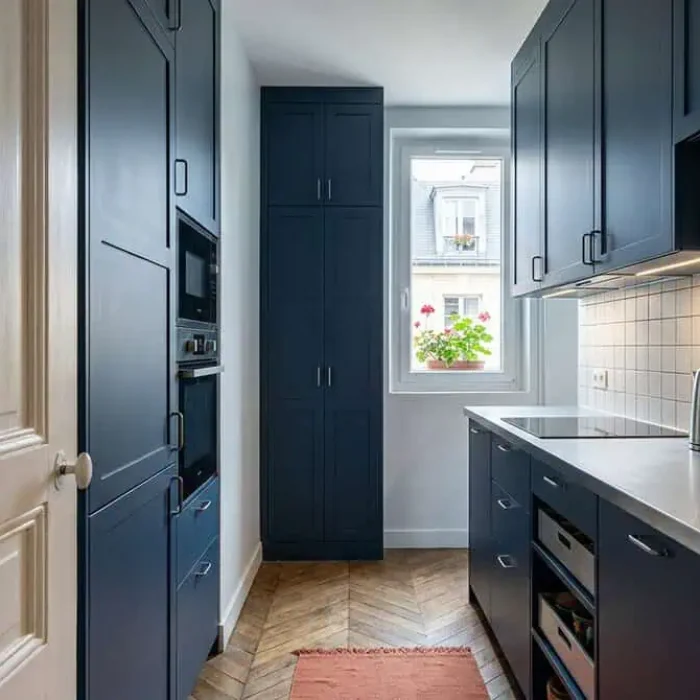 Petite cuisine fermée bleu nuit avec colonne de rangement, plan de travail dégagé et étagères pratiques